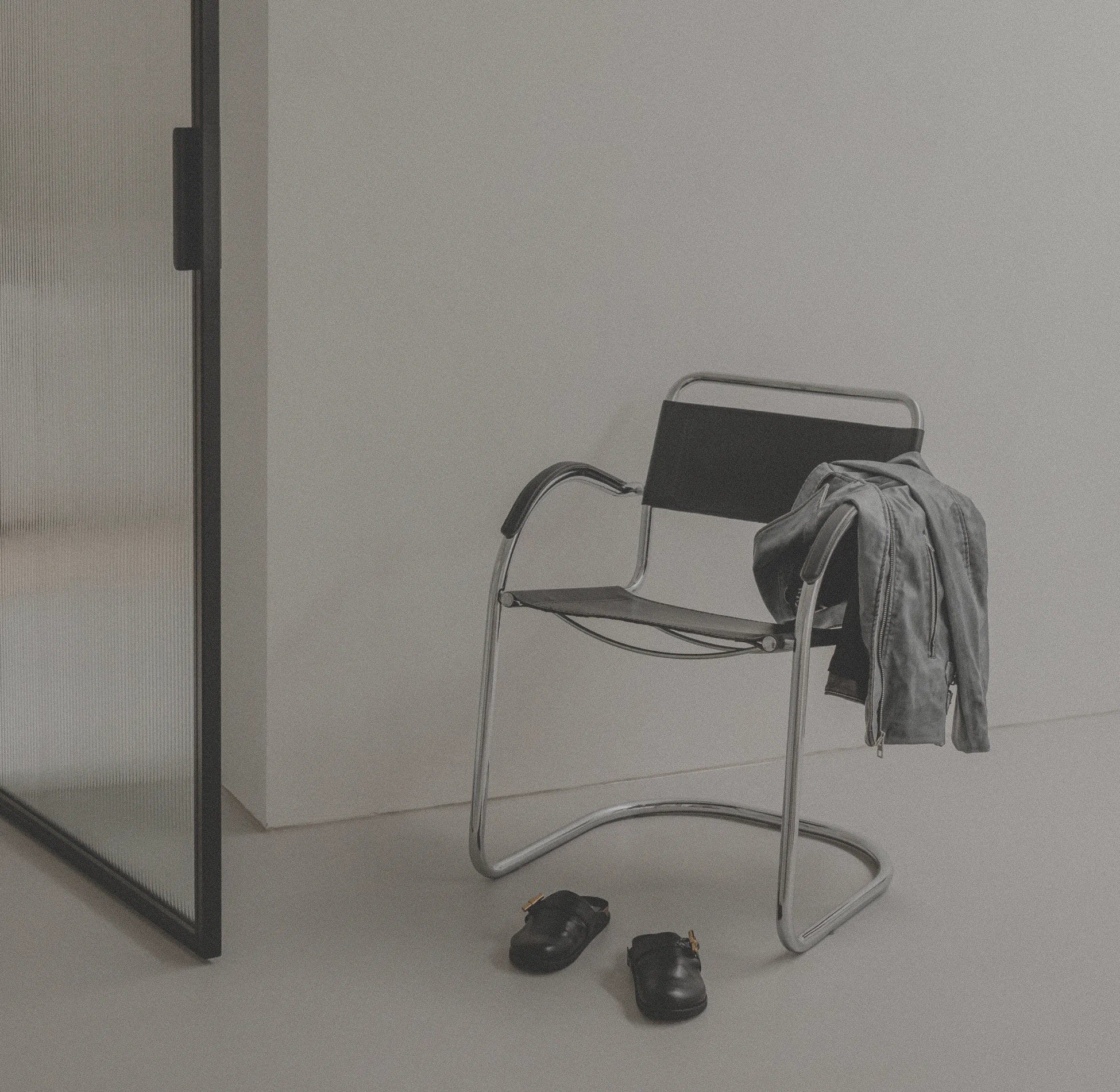 Chair with a jacket draped over it next to a glass door in a minimalistic room.